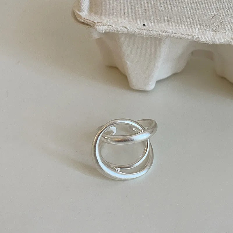 Matte metal open ring with three-dimensional interlaced geometric design in gold or silver finish.