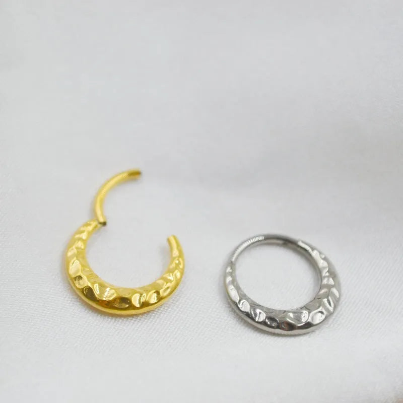 Close-up of a titanium alloy concave-convex nose ring in gold finish, showing carved detail and ring shape.