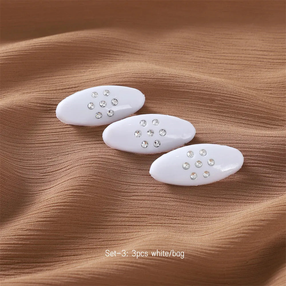 Three plastic plum blossom shaped safety pin brooches with imitation diamond finish on a light background