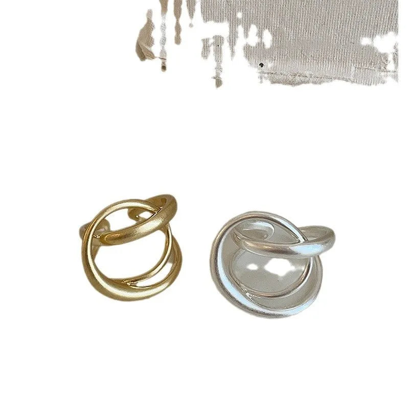 Matte metal open ring with three-dimensional interlaced geometric design in gold or silver finish.