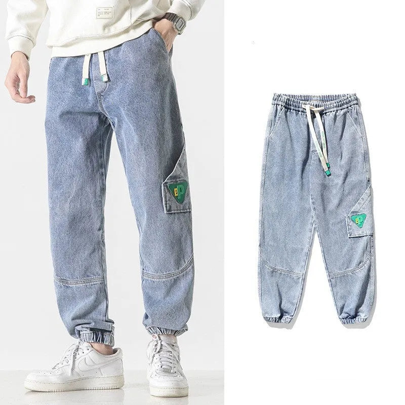 Men's black loose-fit tapered cotton trousers on a hanger, showing the mid-waist and tapered leg design.