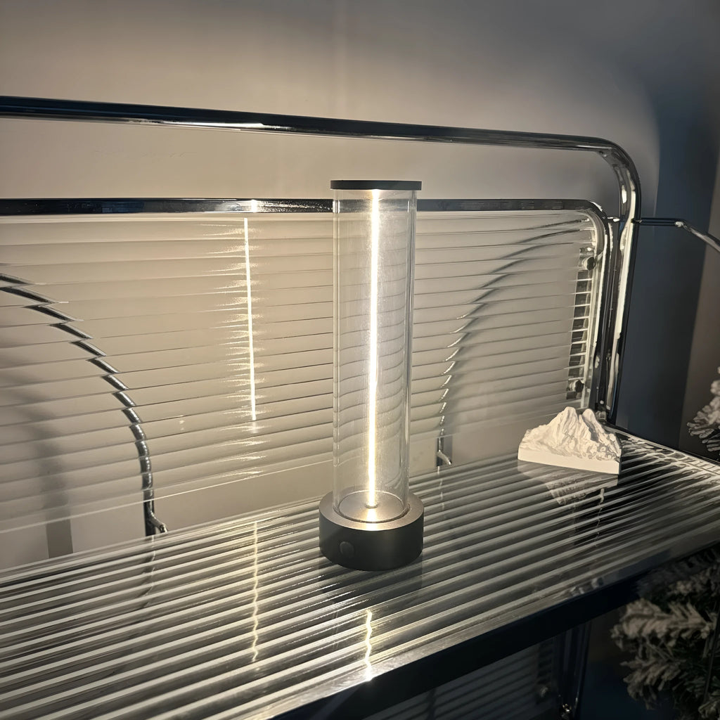 Glass cylindrical LED night light with magnetic base on a metal surface, showing USB charging port.