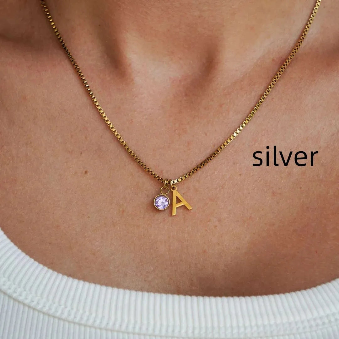 Gold coloured titanium steel birthstone initial pendant necklace with O-ring chain on white background