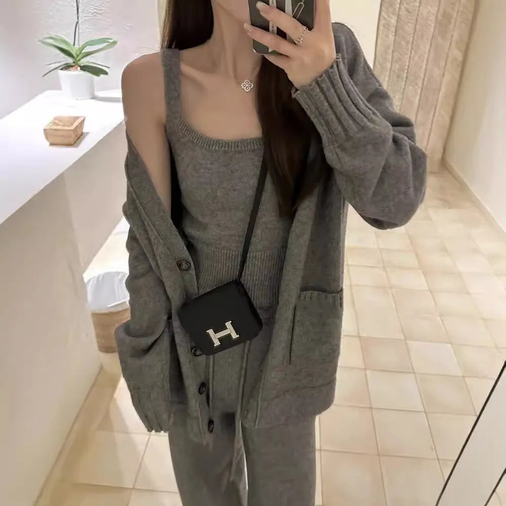 Women's beige knitted cardigan three-piece set with sleeveless vest and suspender trousers on a hanger.
