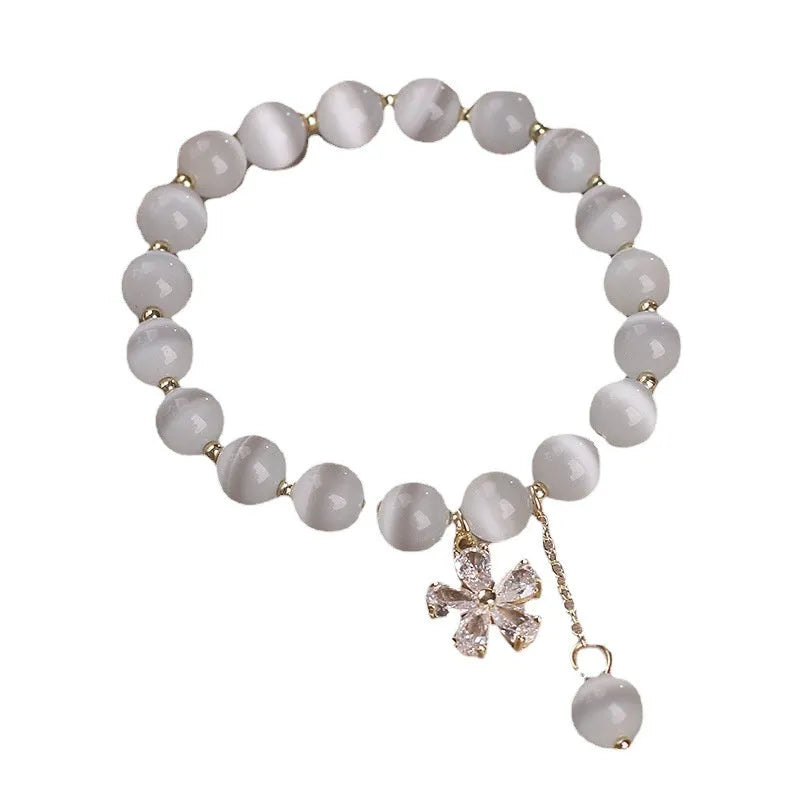 White cat's eye stone flower bracelet with silver-tone details and a hanging tassel charm.