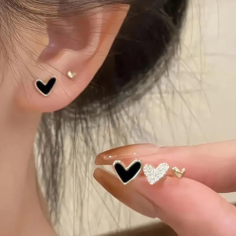 Three pairs of heart-shaped electroplated alloy earrings in gold, black, black and white, and pink colour finishes