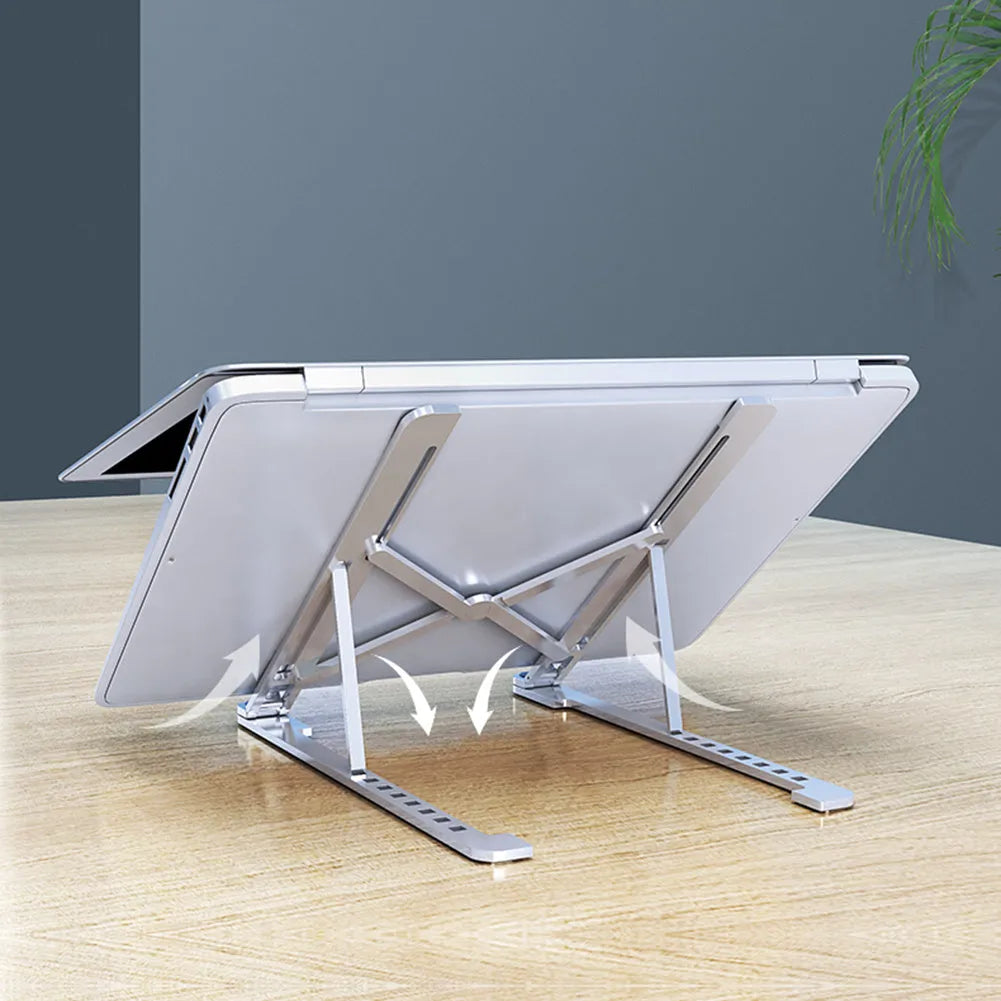 A folded aluminium laptop stand in silver next to an open laptop, demonstrating its compact size.