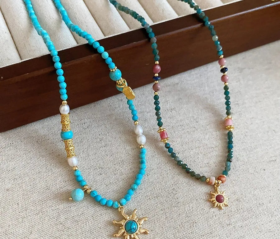 Close-up of a freshwater pearl and geometric stone sun necklace on an adjustable clavicle chain.
