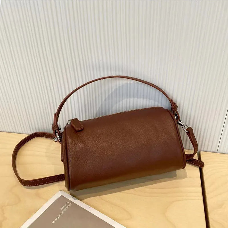 Vegetable-tanned leather crossbody phone bag with cylindrical shape and visible sewing thread detailing