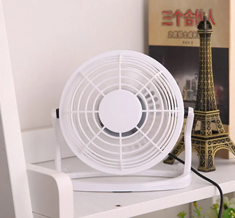 Mini black USB desk fan with adjustable angle on wooden desk next to laptop