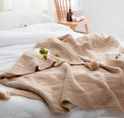 Acrylic knitted blanket with fringed edges in a neutral colour on a sofa.