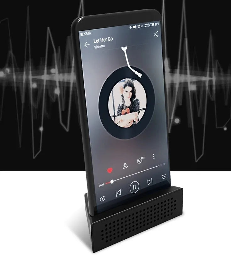 A portable black ABS plastic phone amplifier holder on a desktop, showing a mobile phone inserted for sound amplification.