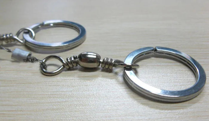 Close-up of a coiled stainless steel survival wire saw with metal pull rings on a wooden background.