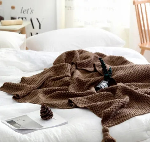 Acrylic knitted blanket with fringed edges in a neutral colour on a sofa.