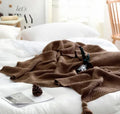 Acrylic knitted blanket with fringed edges in a neutral colour on a sofa.