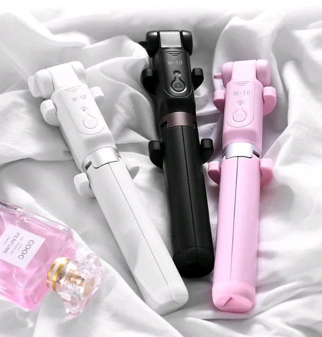 Black Bluetooth selfie stick with extended tripod legs and remote control next to a mobile phone.