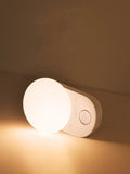 White Baseus rechargeable motion sensor night light with LED glow, shown on a bedside table.