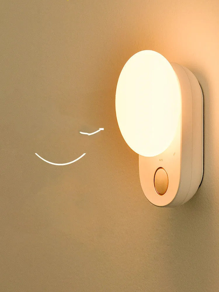 White Baseus rechargeable motion sensor night light with LED glow, shown on a bedside table.