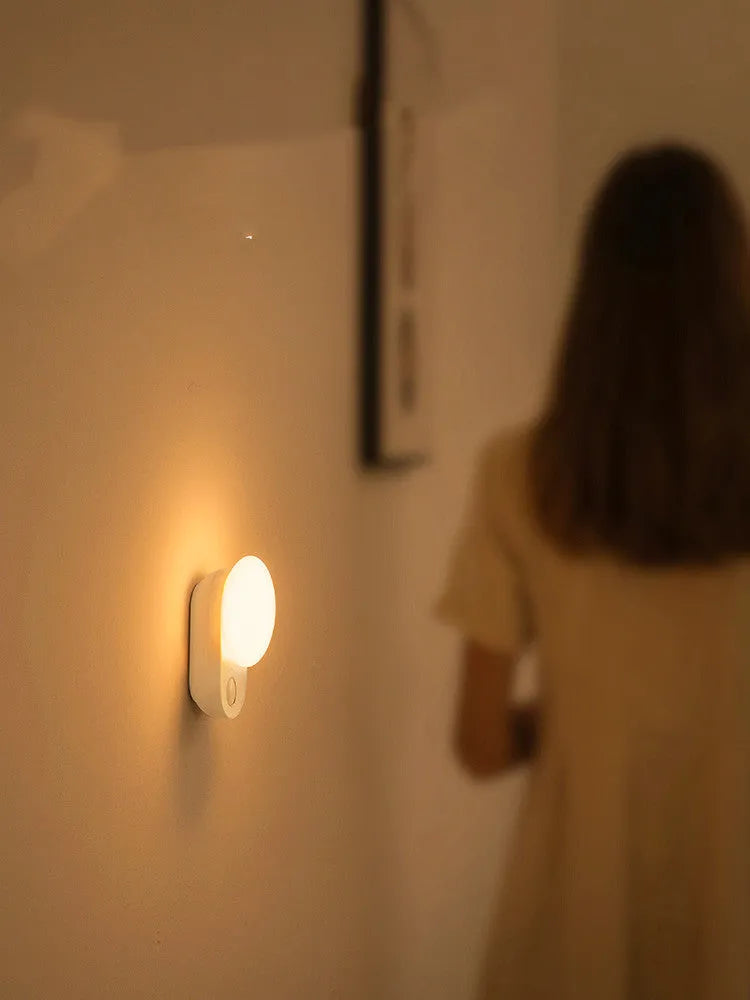 White Baseus rechargeable motion sensor night light with LED glow, shown on a bedside table.