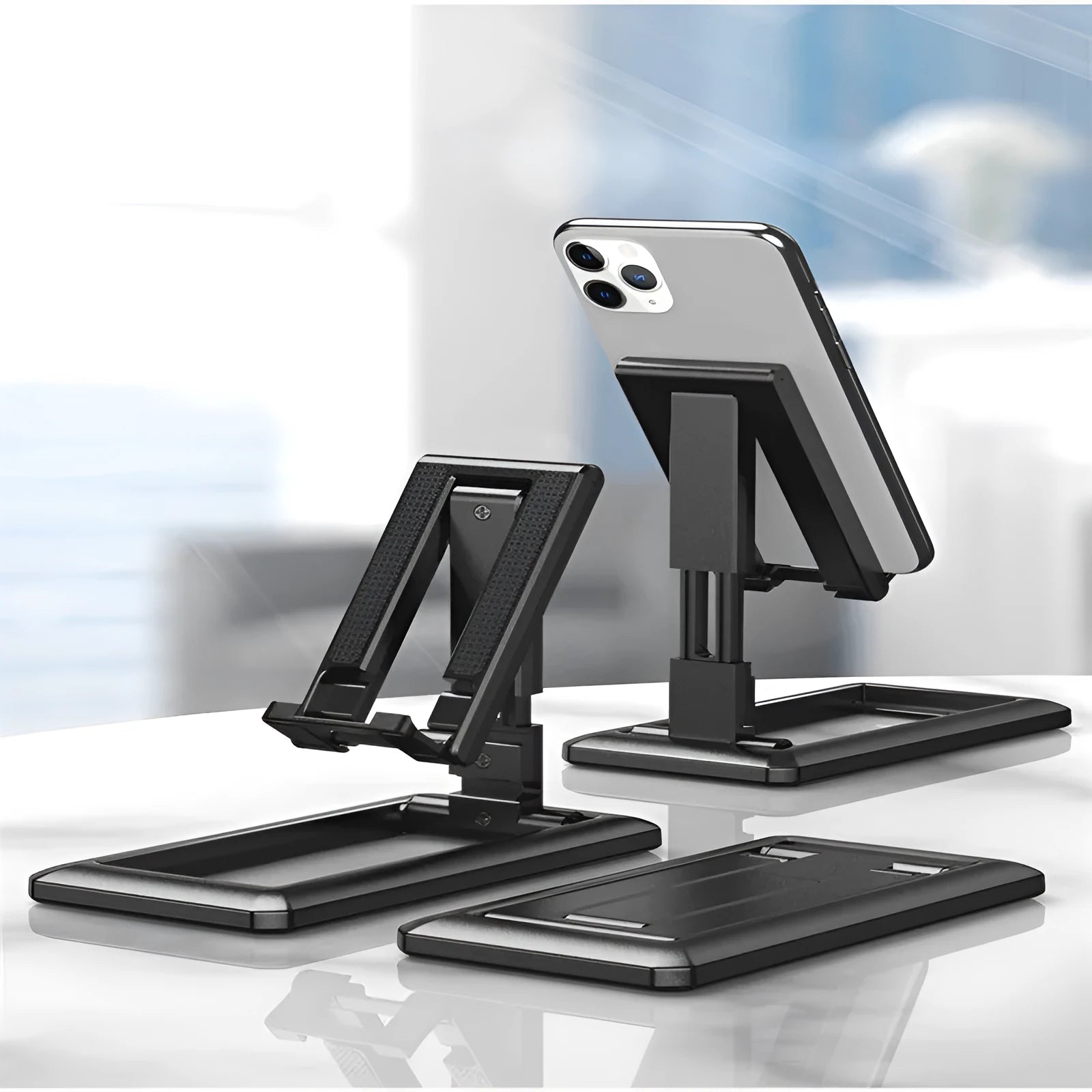 Retractable mobile phone desktop stand in black colour, folded and placed on a desk