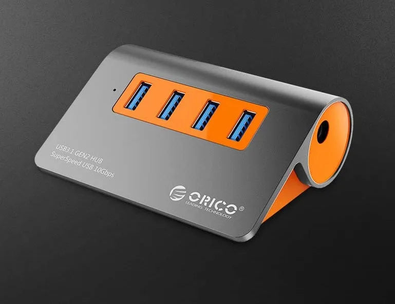 Dark grey aluminium USB hub with orange accents showing four USB 3.1 ports and separate power supply