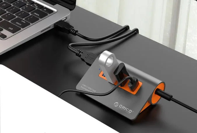 Dark grey aluminium USB hub with orange accents showing four USB 3.1 ports and separate power supply