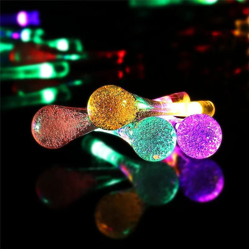 Solar-powered water drop LED string lights in garden with ground spike and bubble pendant design