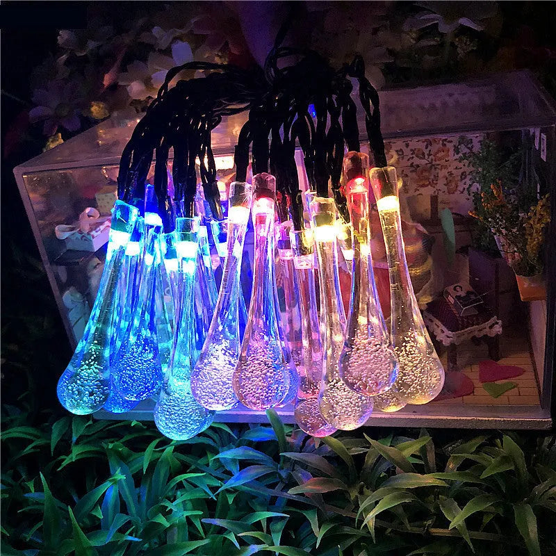 Solar-powered water drop LED string lights in garden with ground spike and bubble pendant design