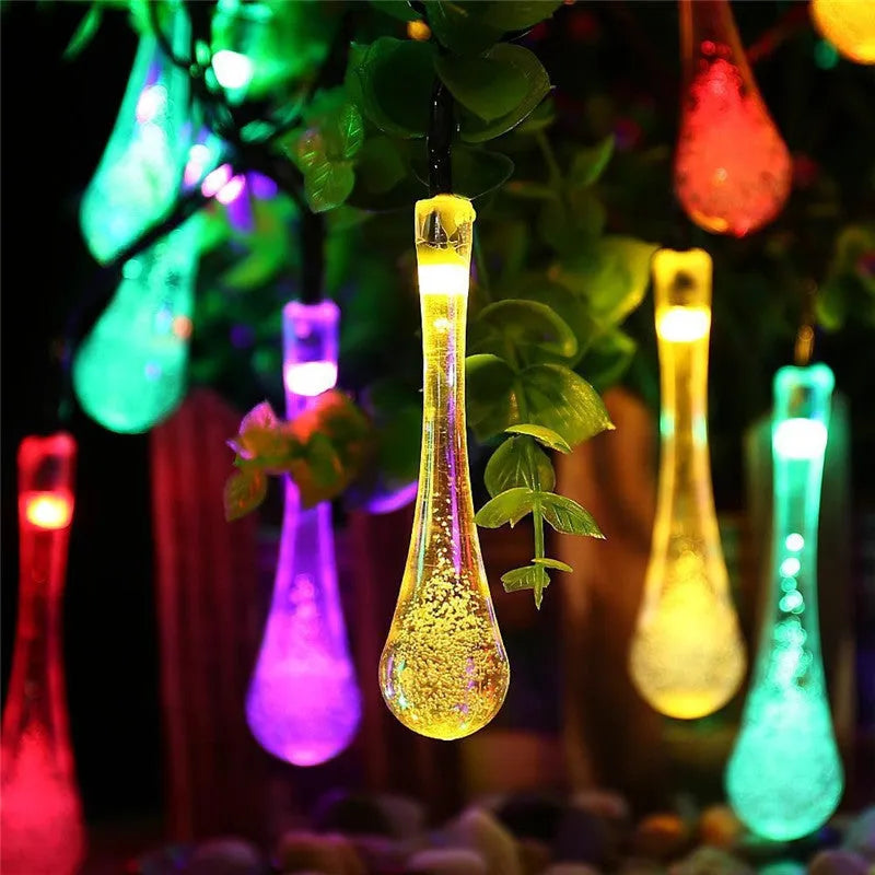 Solar-powered water drop LED string lights in garden with ground spike and bubble pendant design