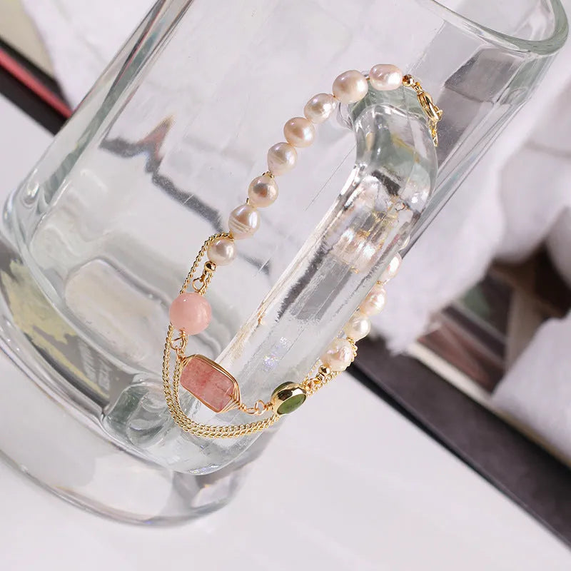 Close-up of a women's pink freshwater pearl bracelet with a geometric strawberry crystal charm on a silver chain.