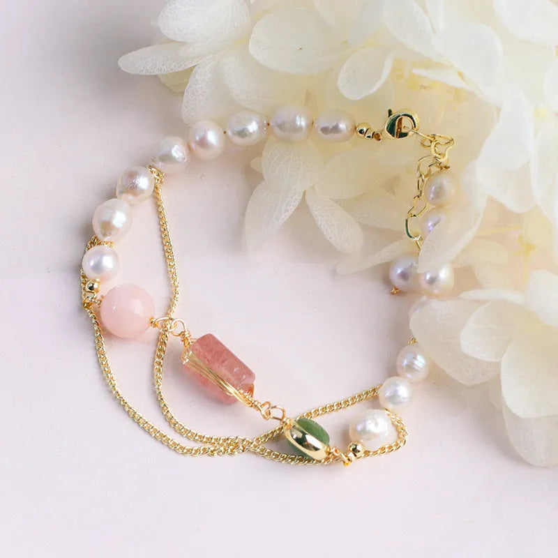 Close-up of a women's pink freshwater pearl bracelet with a geometric strawberry crystal charm on a silver chain.