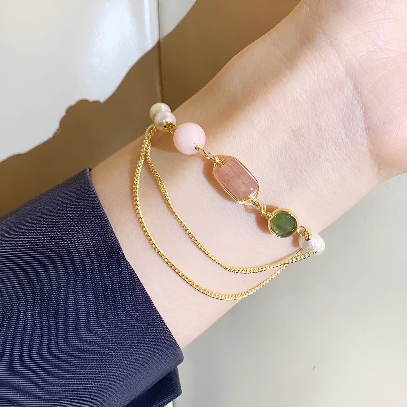 Close-up of a women's pink freshwater pearl bracelet with a geometric strawberry crystal charm on a silver chain.