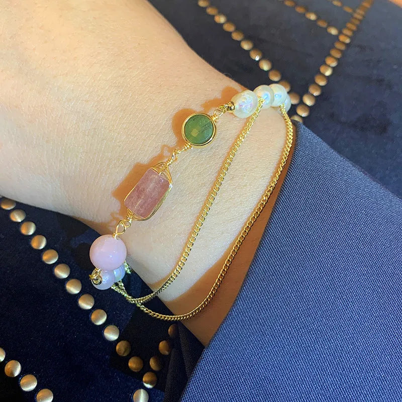 Close-up of a women's pink freshwater pearl bracelet with a geometric strawberry crystal charm on a silver chain.