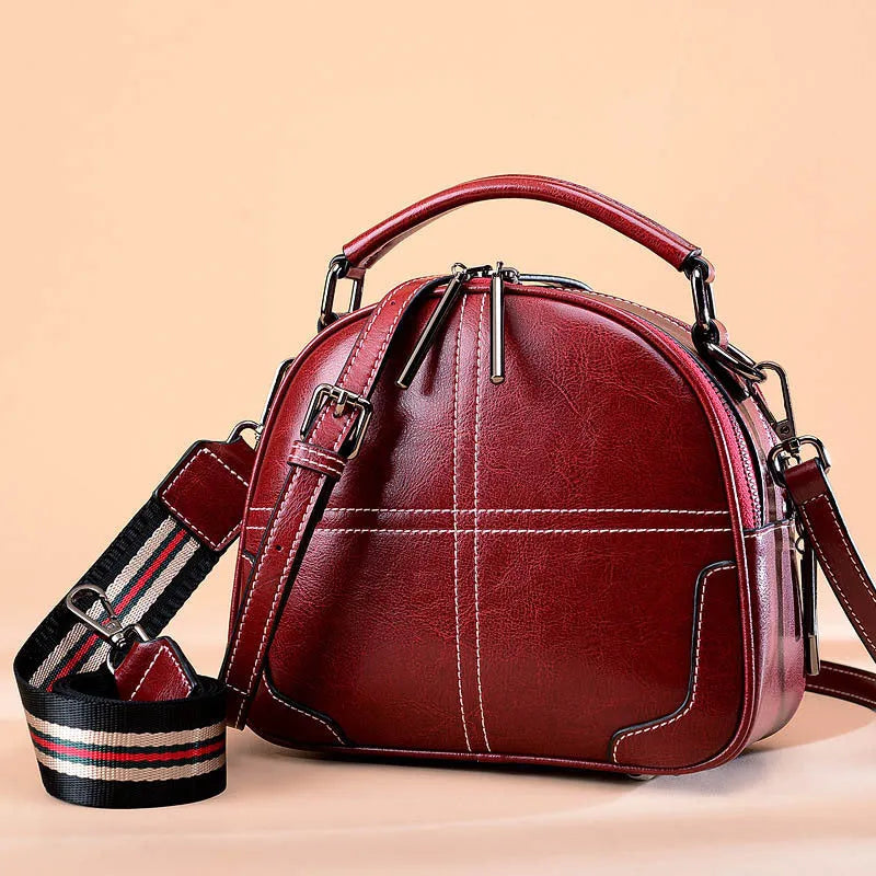 Round leather handbag with zip closure and soft double handles in wine red colour