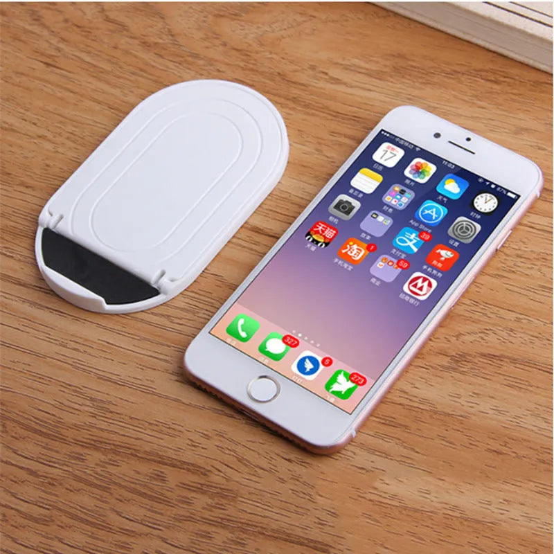 Plastic mobile phone stand with lazy bracket design in six colour options on a table.