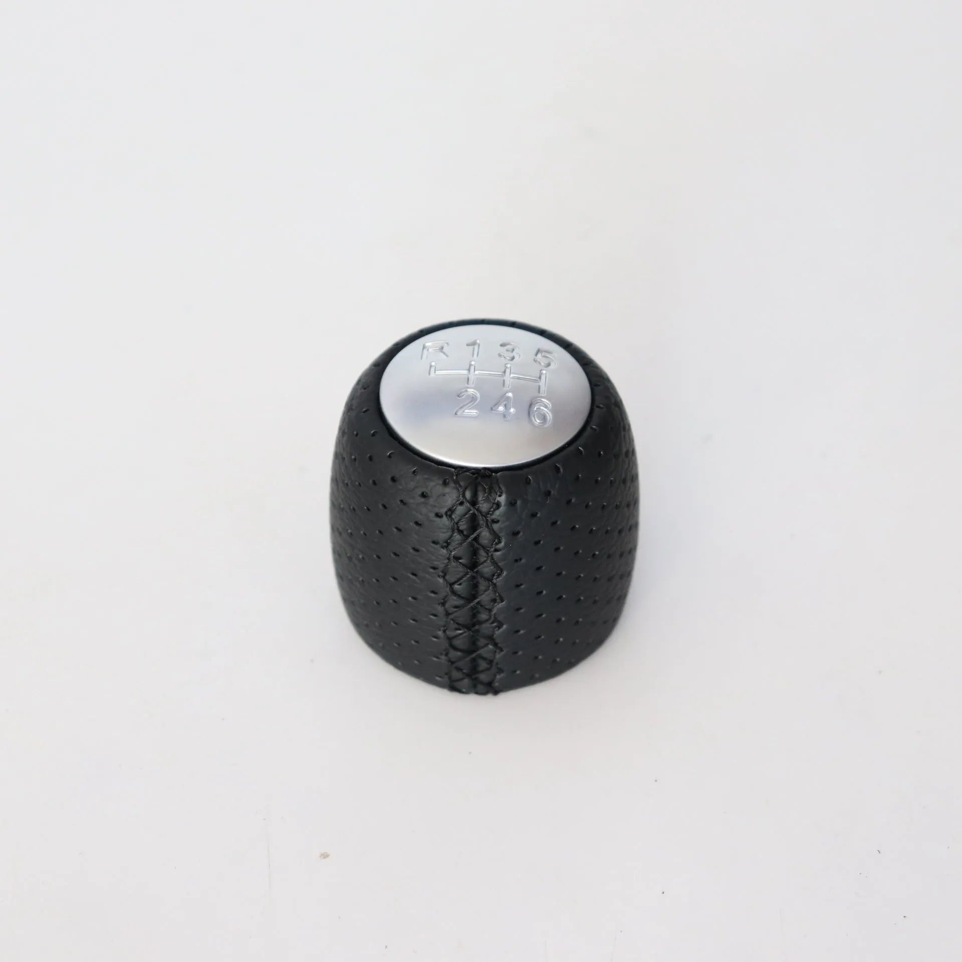 Sewn wrapped black perforated leather gear shift handball for Alpha vehicles on a silver cover.