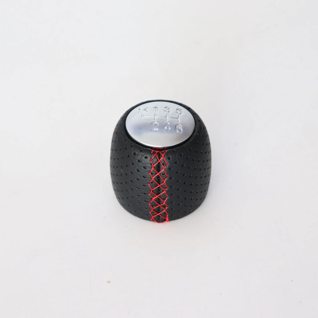 Sewn wrapped black perforated leather gear shift handball for Alpha vehicles on a silver cover.