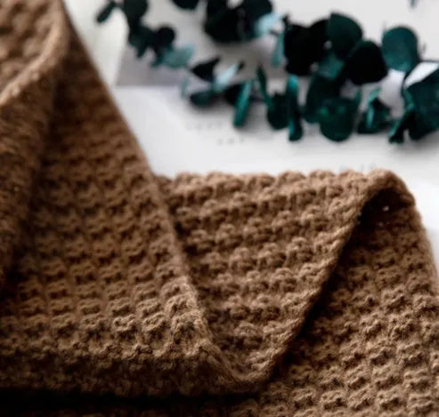 Acrylic knitted blanket with fringed edges in a neutral colour on a sofa.