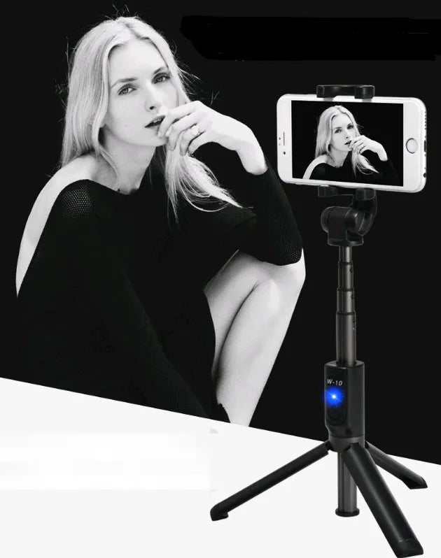 Black Bluetooth selfie stick with extended tripod legs and remote control next to a mobile phone.