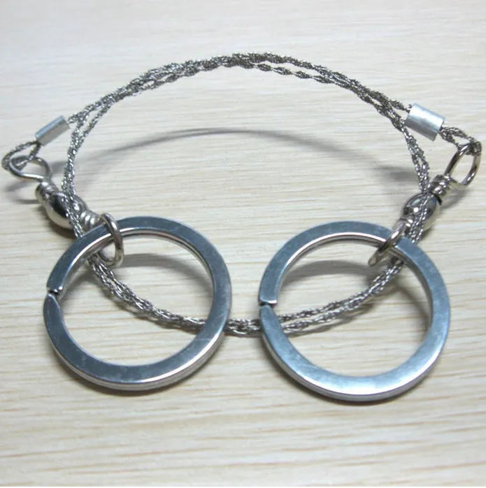 Close-up of a coiled stainless steel survival wire saw with metal pull rings on a wooden background.