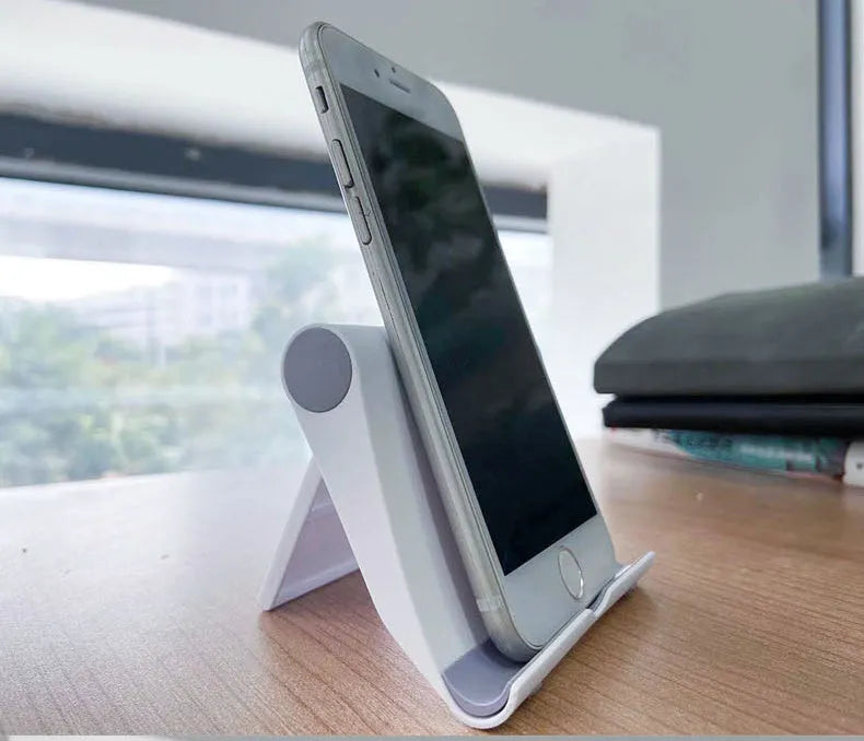 Black PE folding tablet stand holding a mobile phone at an angle on a wooden desk.