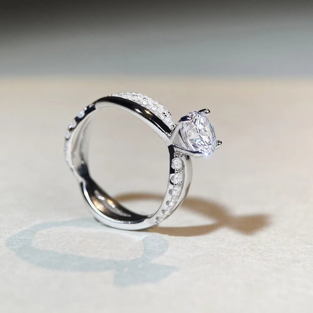 Silver geometric cross ring with a 1 karat moissanite stone in a four-claw setting on a twisted band.