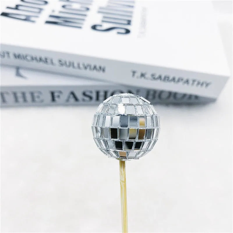 Silver reflective glass disco ball cake topper on a wooden stick for birthday party decoration.