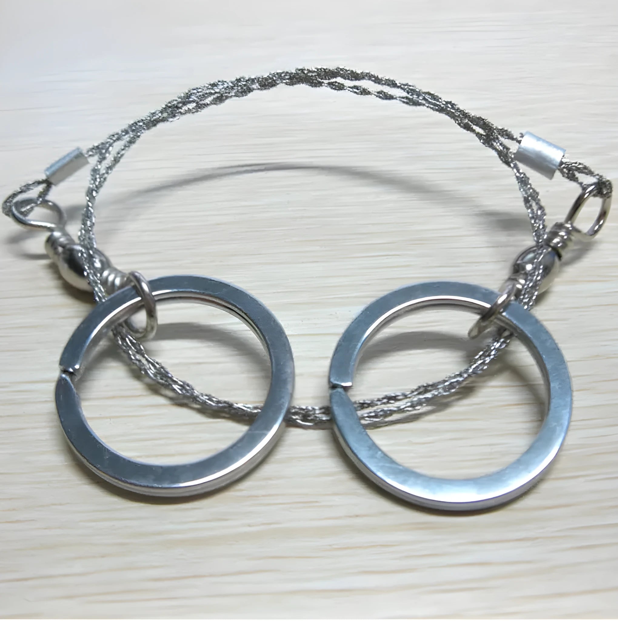 Close-up of a coiled stainless steel survival wire saw with metal pull rings on a wooden background.