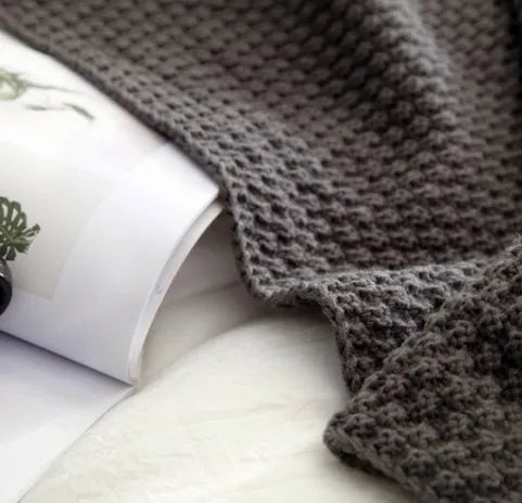 Acrylic knitted blanket with fringed edges in a neutral colour on a sofa.