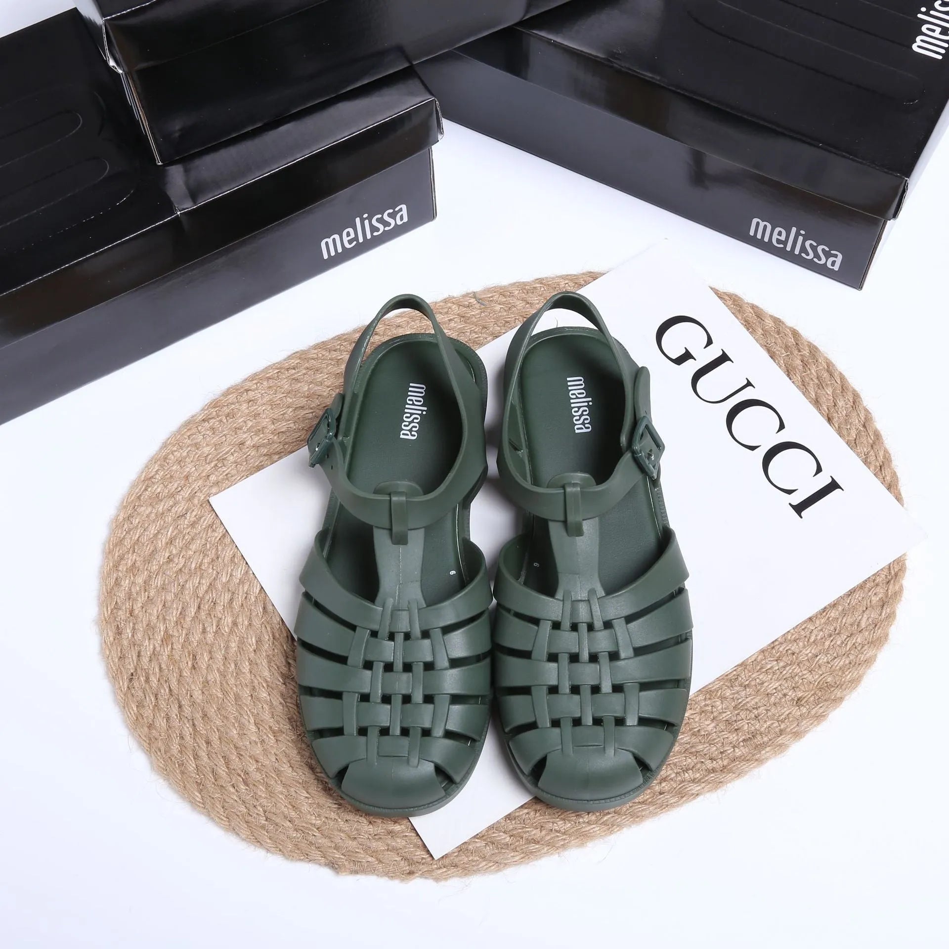 Matte black Roman style sandals with buckle fastening and PVC upper on wooden surface