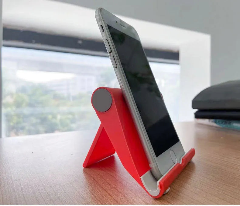 Black PE folding tablet stand holding a mobile phone at an angle on a wooden desk.
