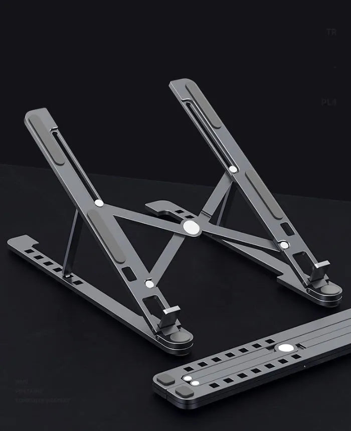 A folded aluminium laptop stand in silver next to an open laptop, demonstrating its compact size.