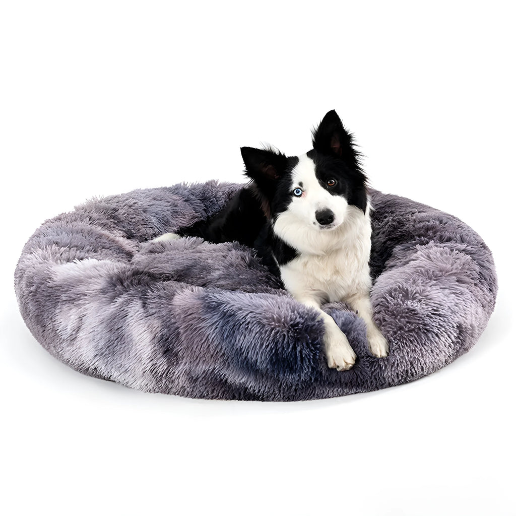 Fluffy donut-shaped dog bed in long plush material, shown in a light grey colour with a raised edge.