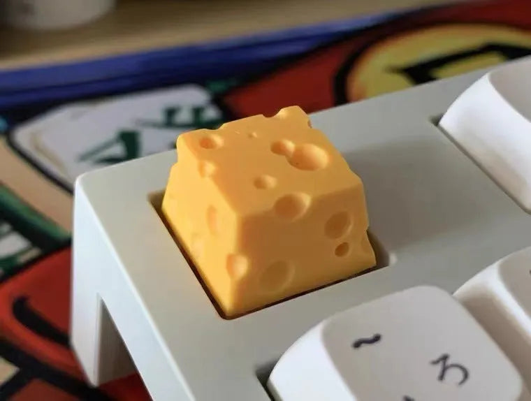 Yellow resin mechanical keyboard keycap shaped like a cheese wedge with a cute character face.